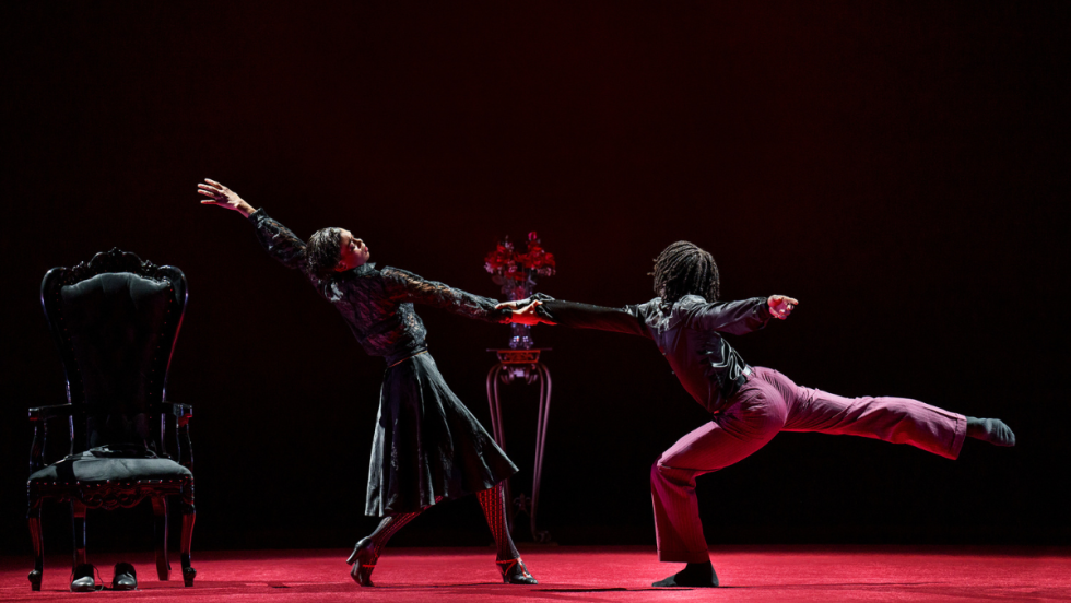 two dancers, a black man and woman - she looks to be pulling away from him - he is in a half crouch with one leg extended behind. he holds one hand as she reaches behind with an extended arm.
