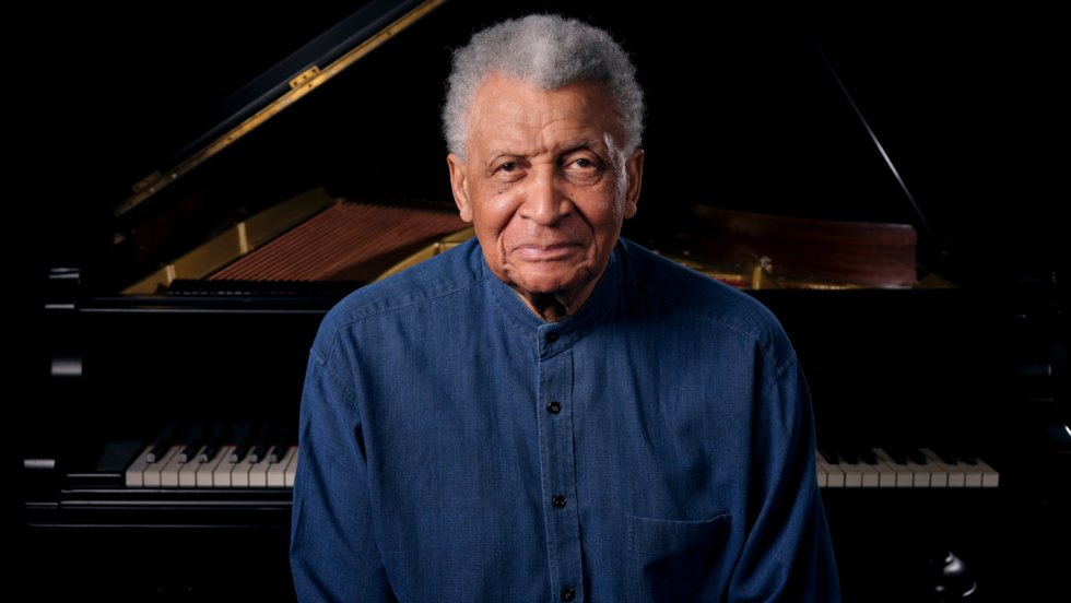 abdullah ibrahim, a multiracial man in his late 80s, sits at the keys of a grand piano