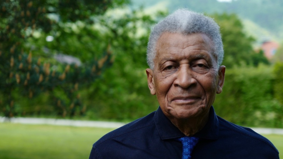 abdullah ibrahim outdoors, in front of a meadow and tree-covered hills
