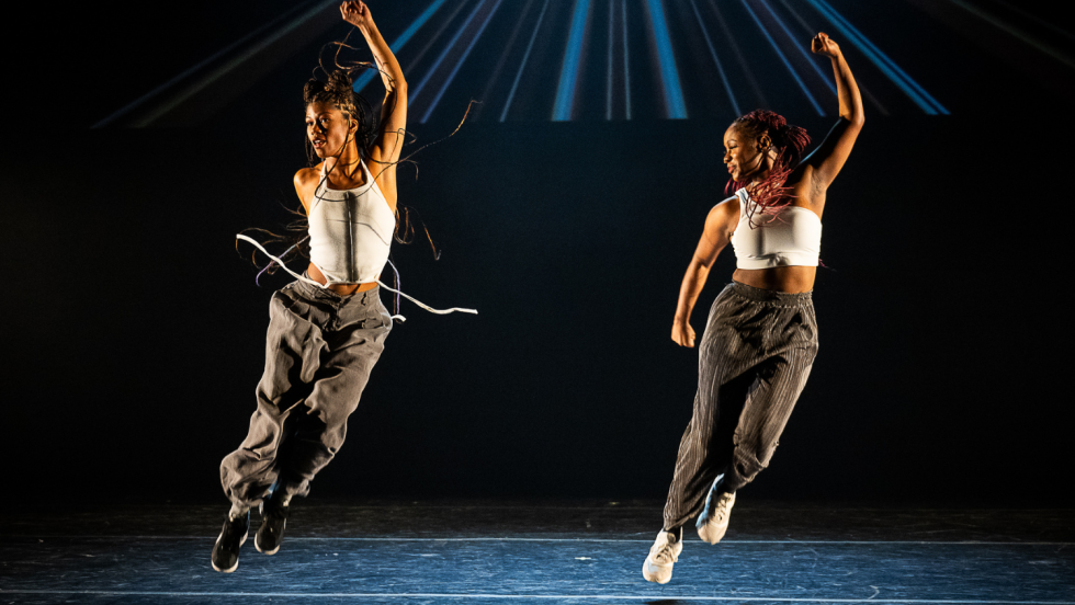 two women, skip in unison, their left arm raised in a fist