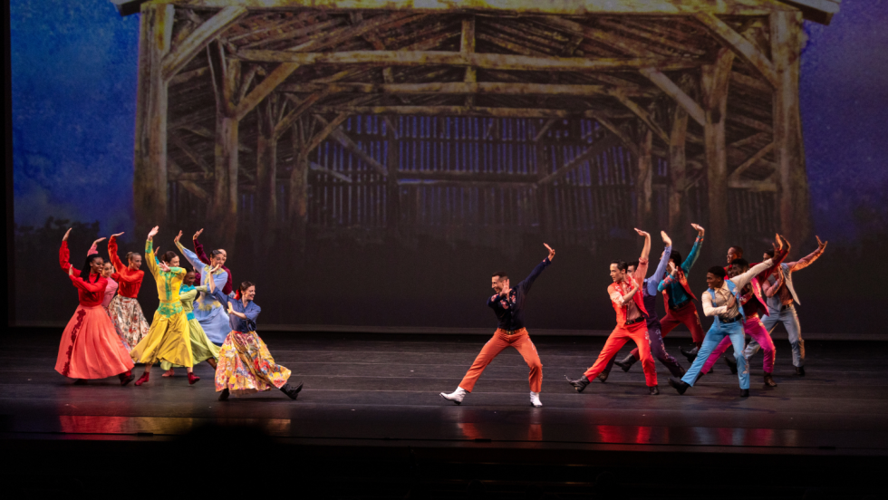 in a scene resembling a barn, female dancers gather on the left and male dancers on the right