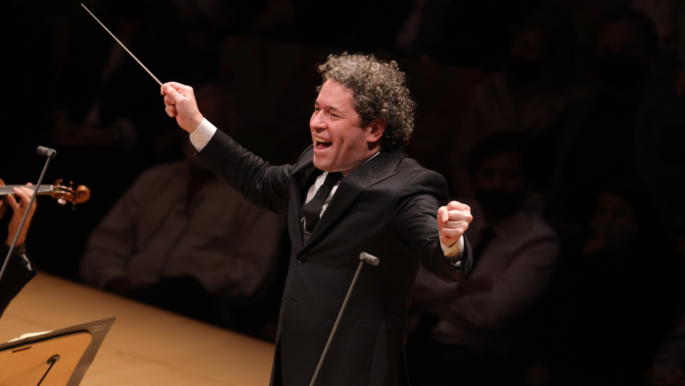 a man with curly dark hair smiles broadly as he conducts a symphony orchestra