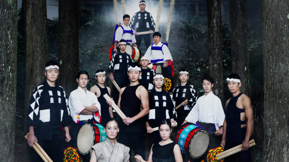 members of the Kodo ensemble, in a misty woods, stand together holding drumsticks