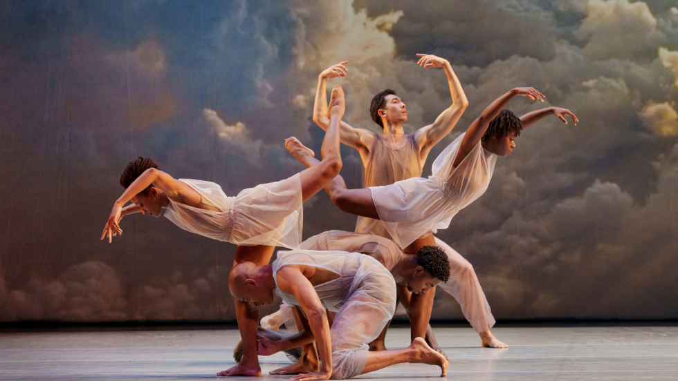 with curved arms and legs, and arced bodies, a diverse company of dancers pose in front of a backdrop of clouds touched with heavenly golden light.