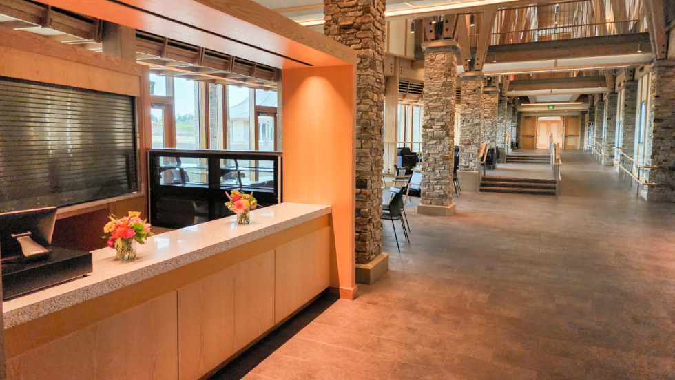 a bar in a bright empty theatre lobby, made of light natural wood with a natural stone floor. 