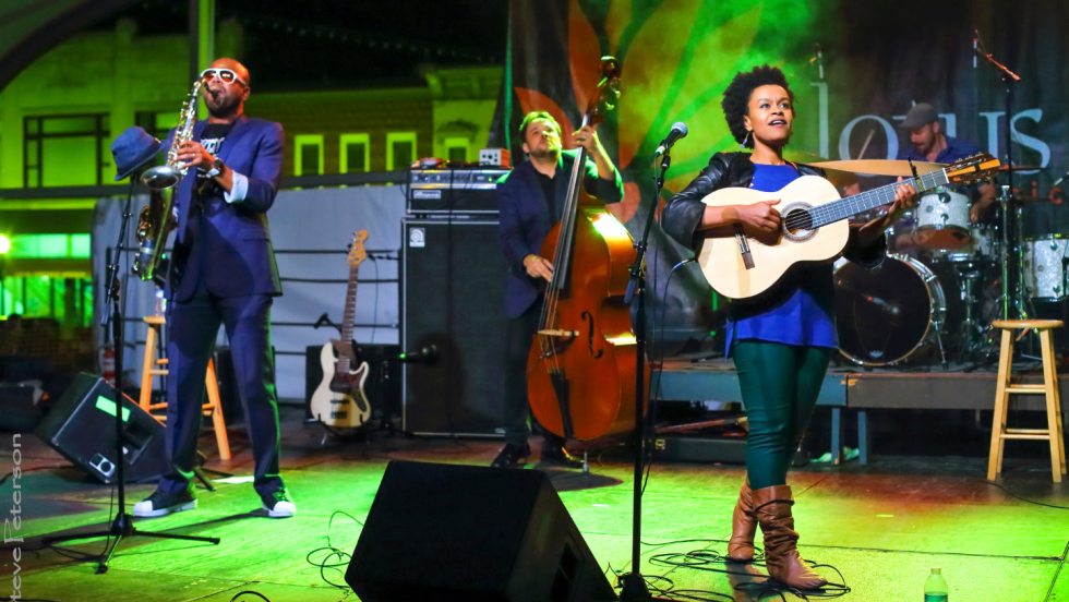 Meklit plays guitar with her band on a green-lit stage with a puff of haze behind them