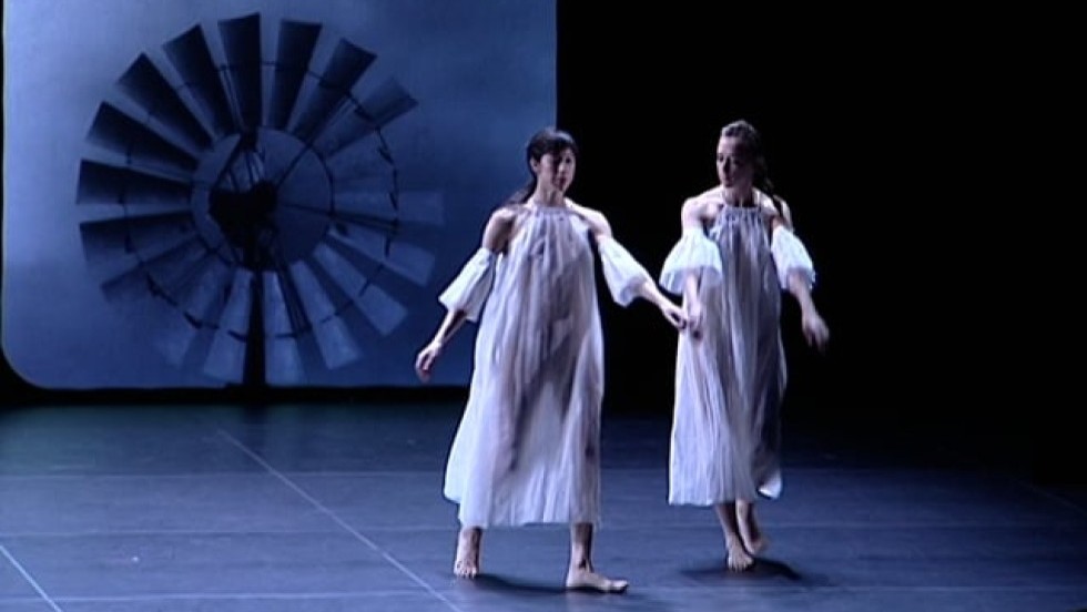 Dancers in sheer dresses glide across the stage before projected modern art photographs. There is no musical soundtrack to the piece.