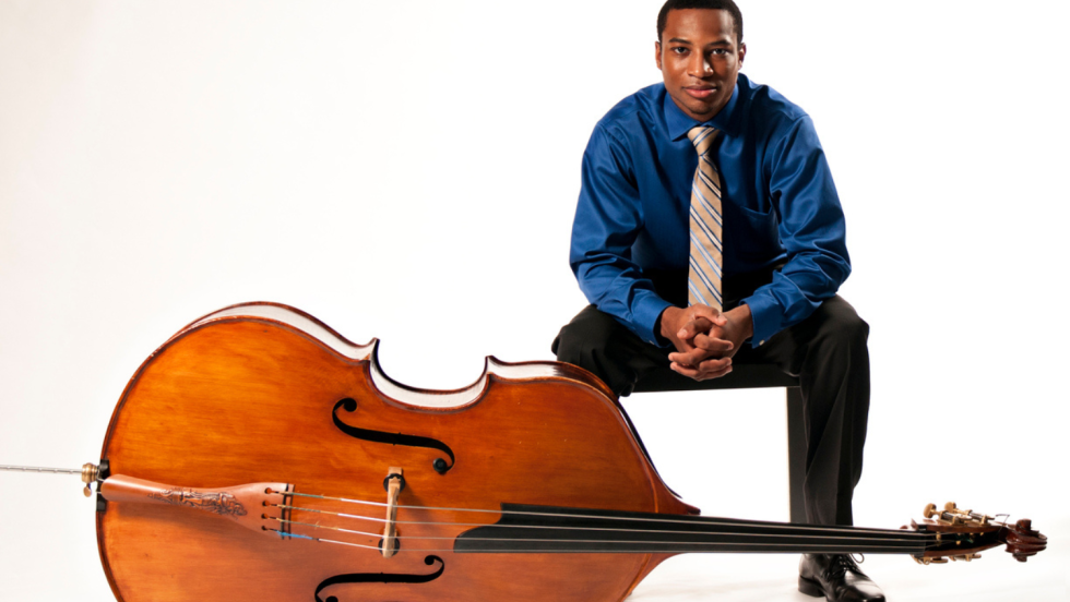 bassist xavier foley sits on a square stool, his bass laid on its side at his feet