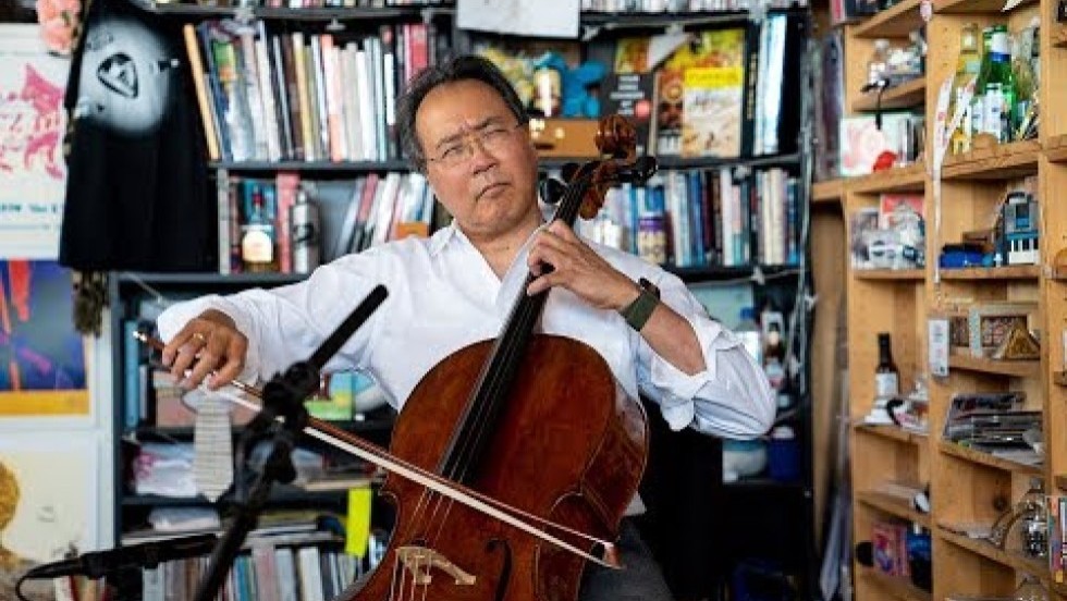 cellist yo-yo ma performs at NPR's Tiny Desk, surrounded by tightly packed shelves of books, records, and pop culture/fandom knickknacks