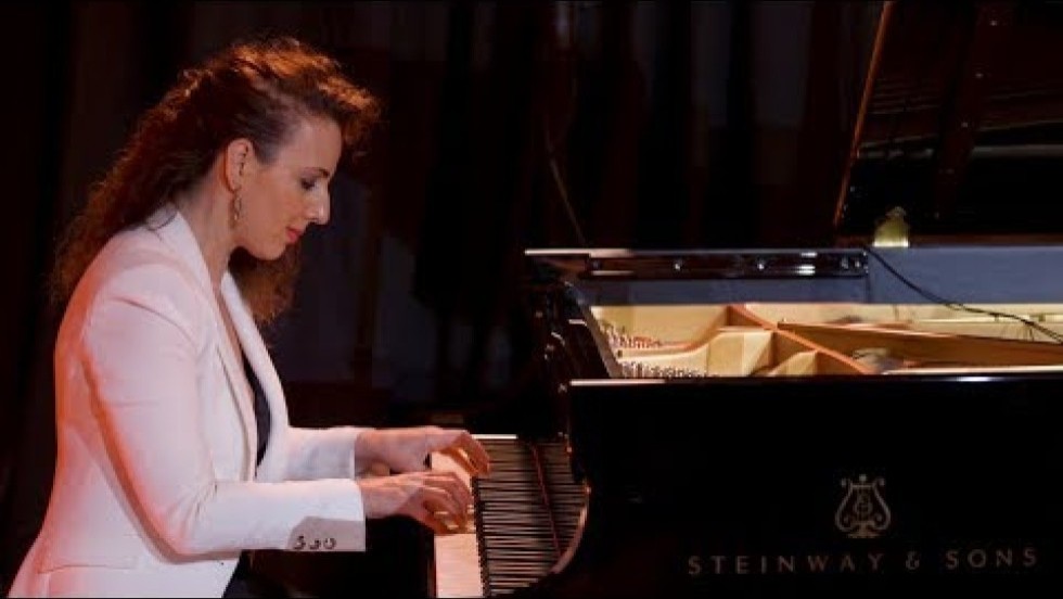 a solo pianist in dark clothing with a bright white jacket performs on a grand piano