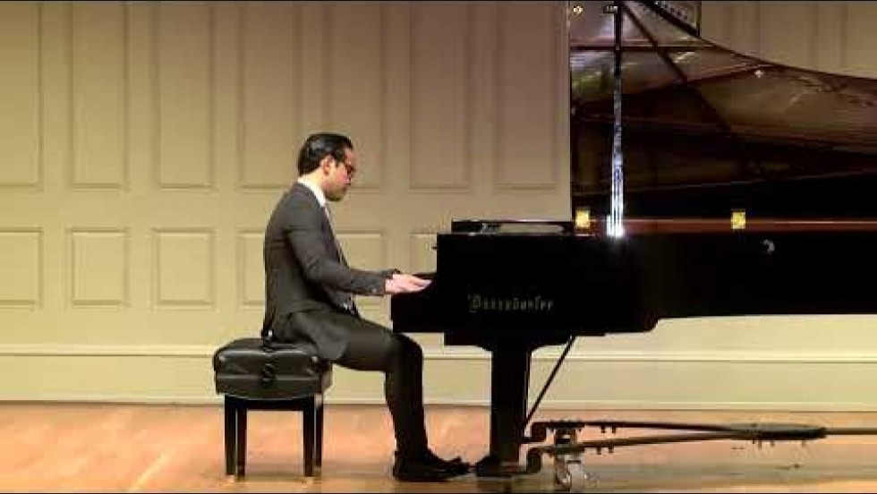 a latino man performs on a grand piano on stage in a concert hall