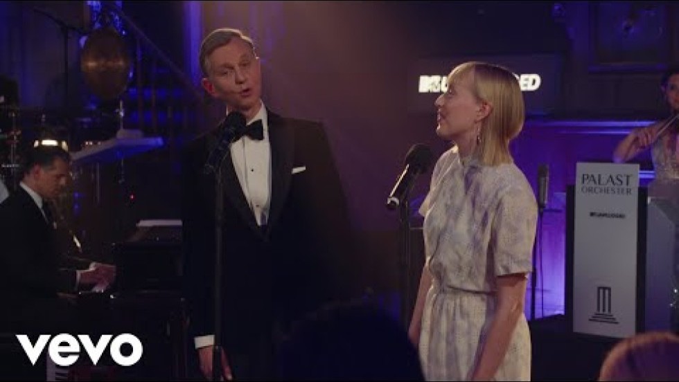 a big band, a blonde white female singer with heavy bangs, and a white male singer with slicked-back gray hair and an elegant suit