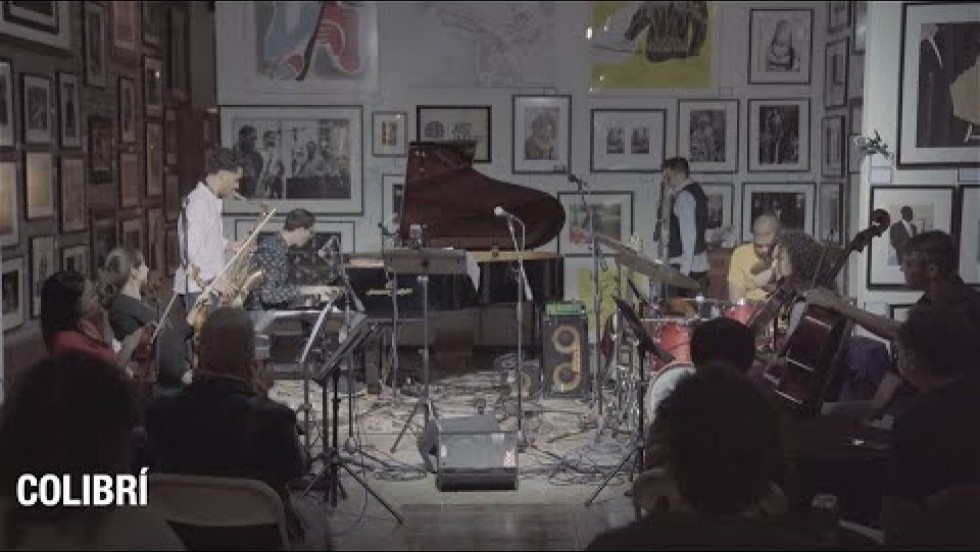 a band plays on a small stage lined with framed photographs of musicians