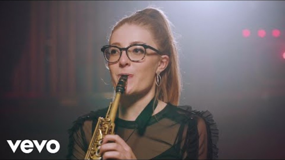 a young brown-haired white Englishwoman plays the soprano sax in a dimly lit and hazy nightclub that evokes a Parisian or European setting