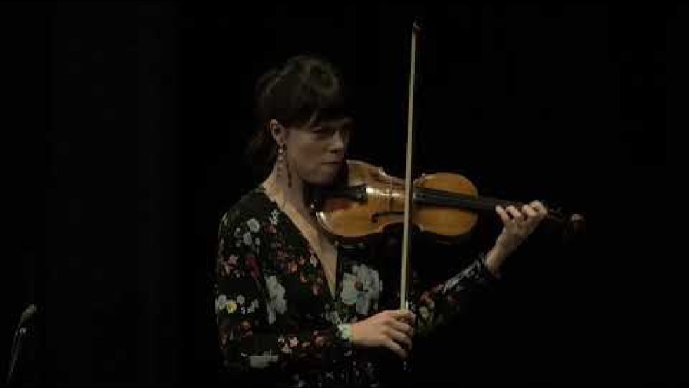 a violinist, a bassist, and a cellist perform on a dark stage