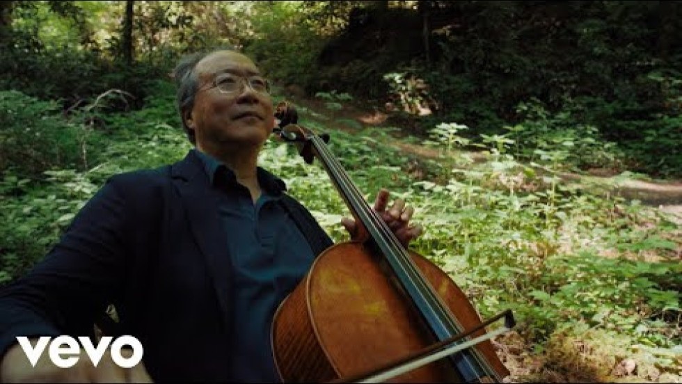 Yo-Yo Ma performs Bach's first cello suite near a stream surrounded by green trees and ferns