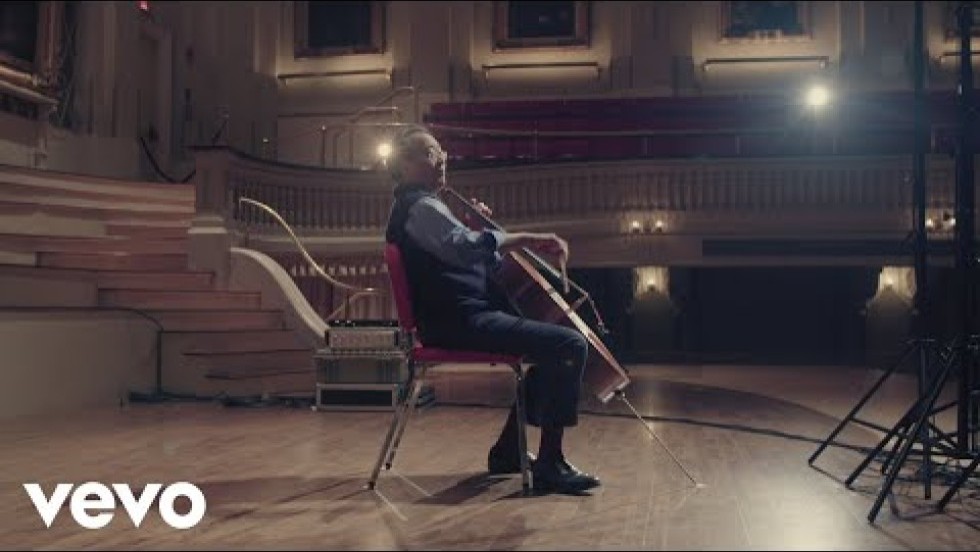 Yo-Yo Ma performs on an empty concert stage in a wood-paneled hall