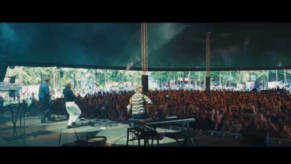 a folk trio plays for an excited crowd in a large concert pavilion at a large music festival