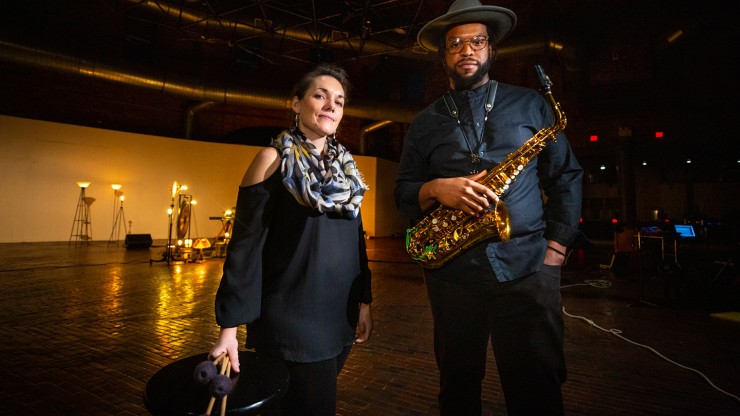 A white woman holding mallets and a black man holding a saxophone