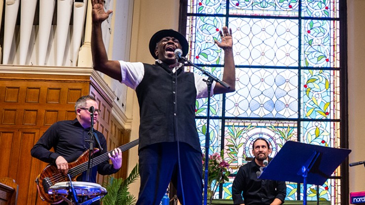 A poet performs with a band, his arms raised mid-exclamation