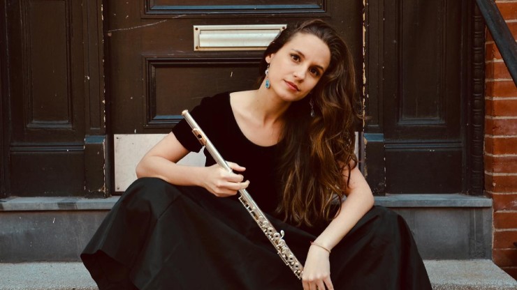 a young woman with long brown hair sits on a doorstep holding a silver flute