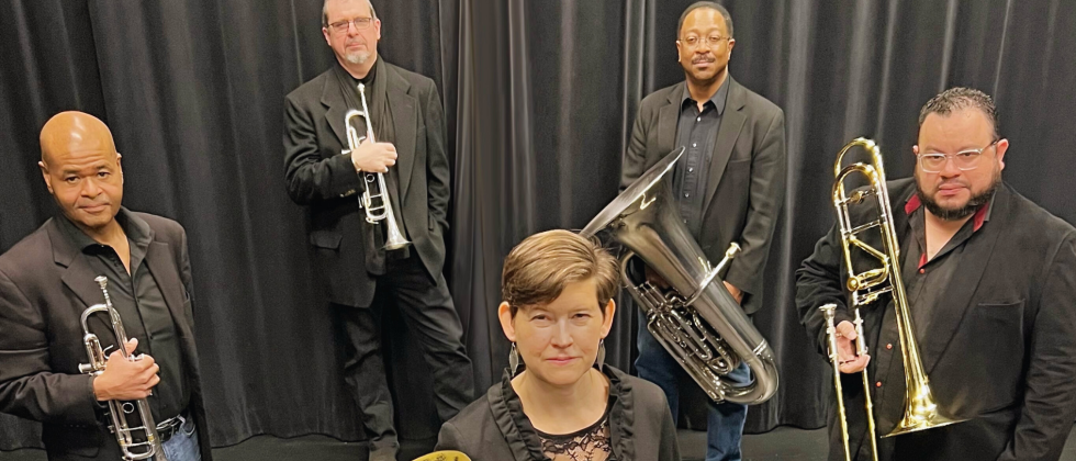 Four men stand in an arch with a white woman standing in front, all holding brass instruments. 