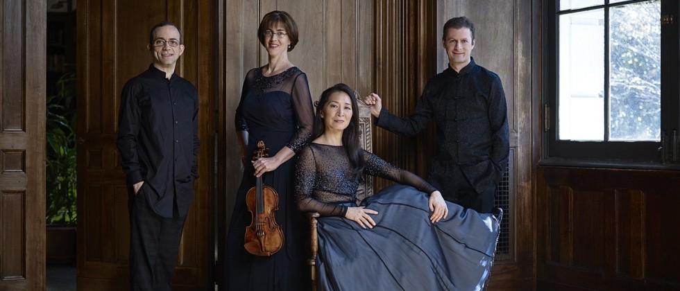the four members of a string quartet, two men flanking two women, inside an ancient mansion. One of the women holds a violin.
