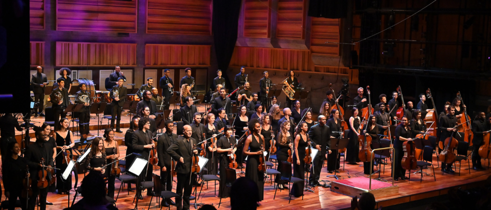musicians from Chineke! Orchestra in black outfits stand on stage, facing the audience for a bow at the end of a concert