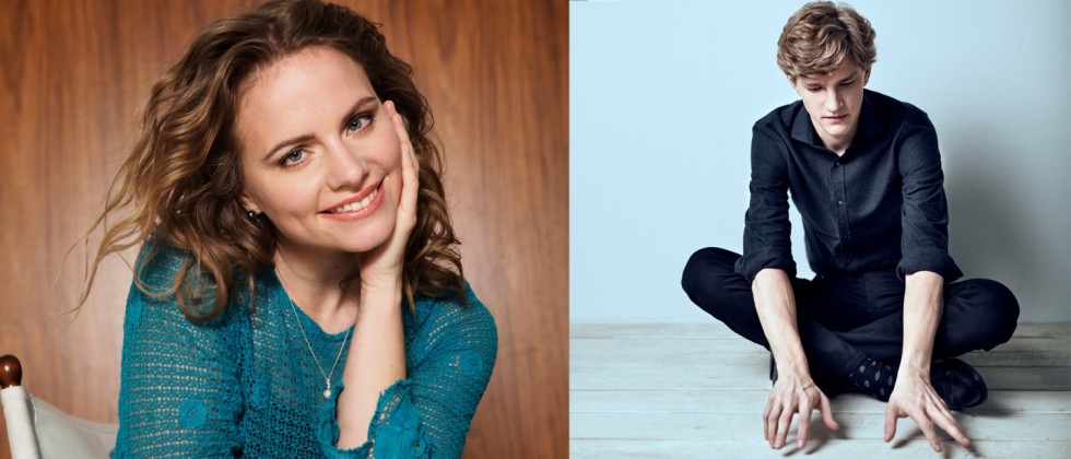 A white woman with brown hair smiles with her face in hand; a man sits with his arms floating just above the ground. 