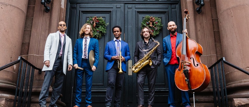 a jazz band with their instruments, in front of the large doors of a historic brown sandstone church
