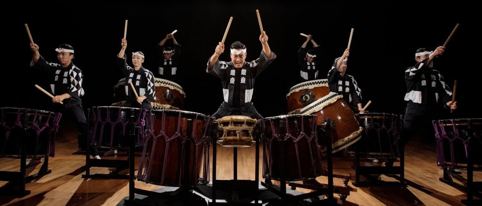 A large group of Japanese musicians perform on their taiko drums. 