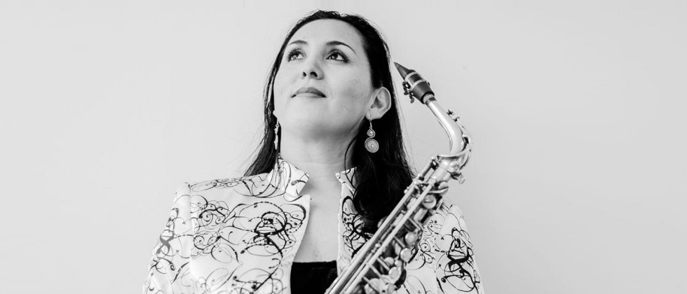 A woman, holding a tenor saxophone, looks up and out of frame.