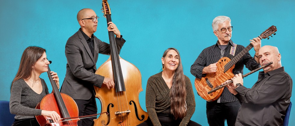 Pan-Latin ensemble with several stringed instruments gathers in front of a teal background in gray performance wear. 