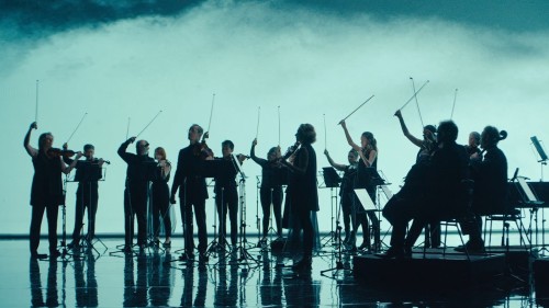 Dark silhouettes of 8 string players appear against a cloudy background, extending their bow arms in the air. 