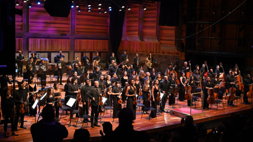 musicians from Chineke! Orchestra in black outfits stand on stage, facing the audience for a bow at the end of a concert