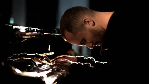 Igor Levit, a white man in a black top plays the piano with his head bowed. 