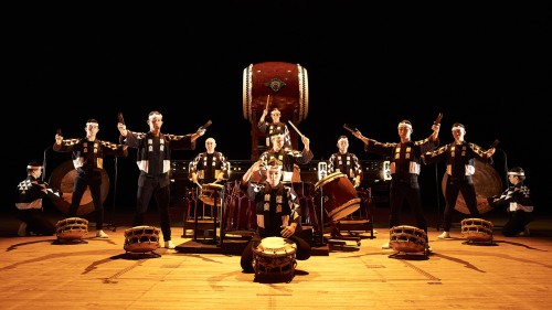 Eleven KODŌ drummers in black and white outfits gather on stage with their instruments.