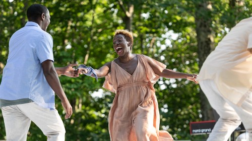 a joyous black woman in motion smiles broadly as she grasps her dance partner's hand