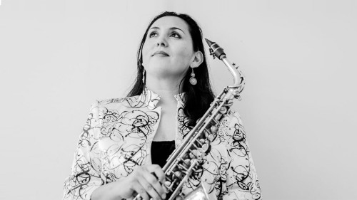 A woman, holding a tenor saxophone, looks up and out of frame.