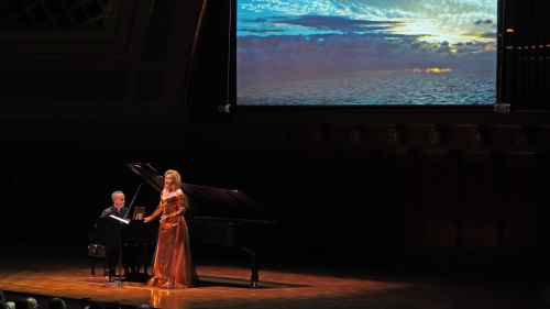 a singer in a copper-colored gown, a pianist, and a film showing a dramatic sky