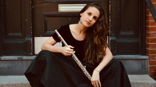 a dark-haired young woman sits on the stoop of a brick building holding a flute