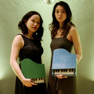 two young asian-american women hold toy pianos in a white room
