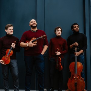 the four young men of the isidore string quartet laugh and smile in front of a blue wall