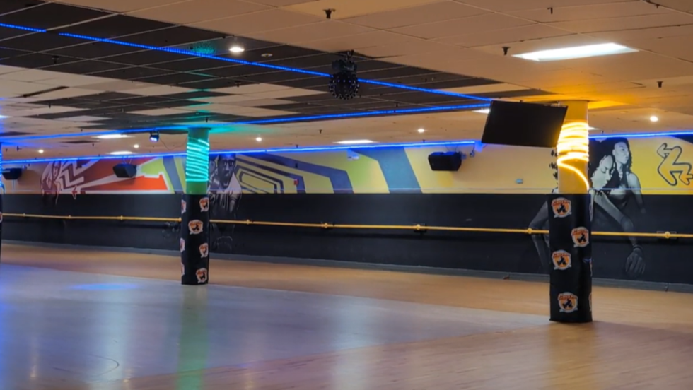 the interior of a roller skating rink, with carpeted columns throughout and a grafitti-inspired mural on the far wall