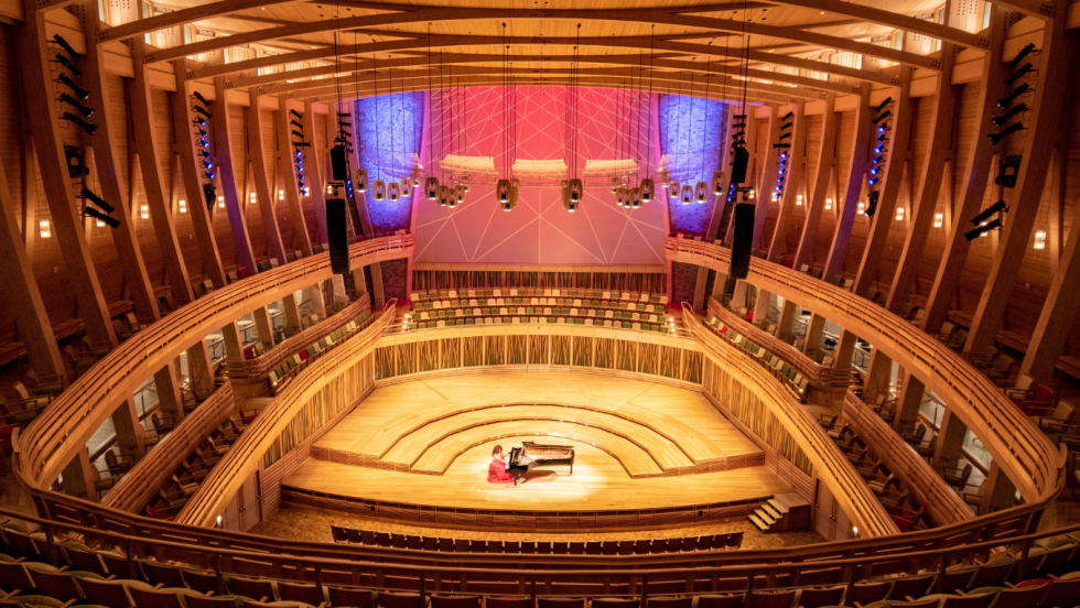 A 1000-seat horseshoe shaped concert hall, paneled in light wood, an organ, lit in red and blue, rises behind the stage