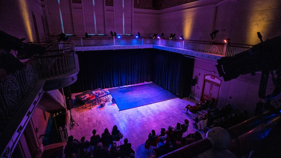 A small room with a balcony and flat wooden stage lit in purple