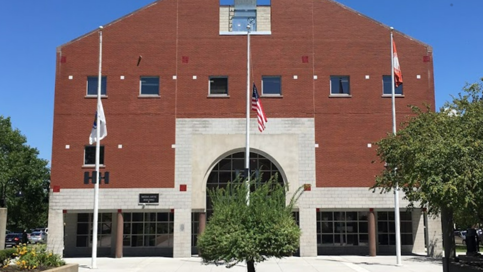 A large brick building with tress and flag poles out front